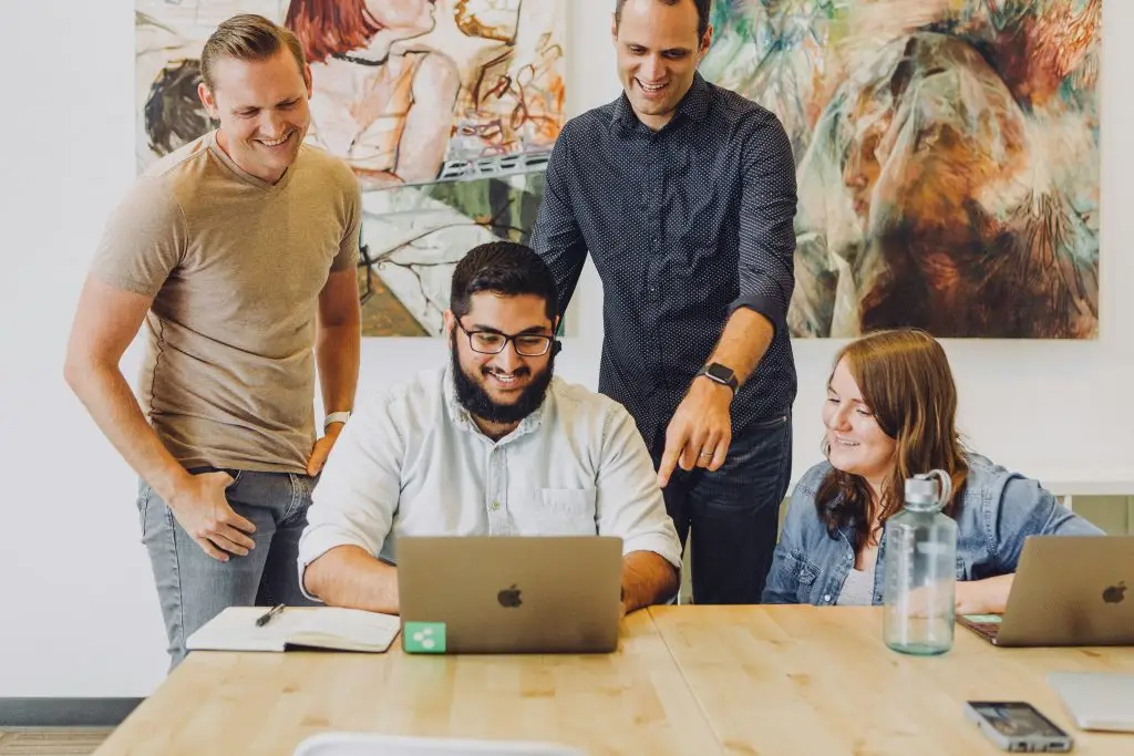 A group of 4 professionals co-working and collaborating while looking at a laptop,